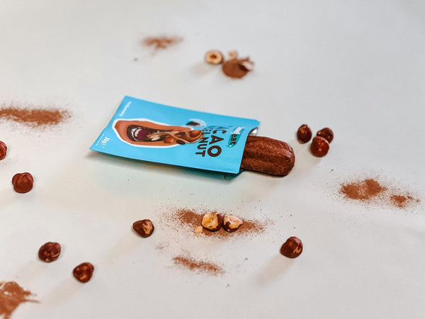 Cacao churro sliding out of its pack among hazelnuts and cacao powder