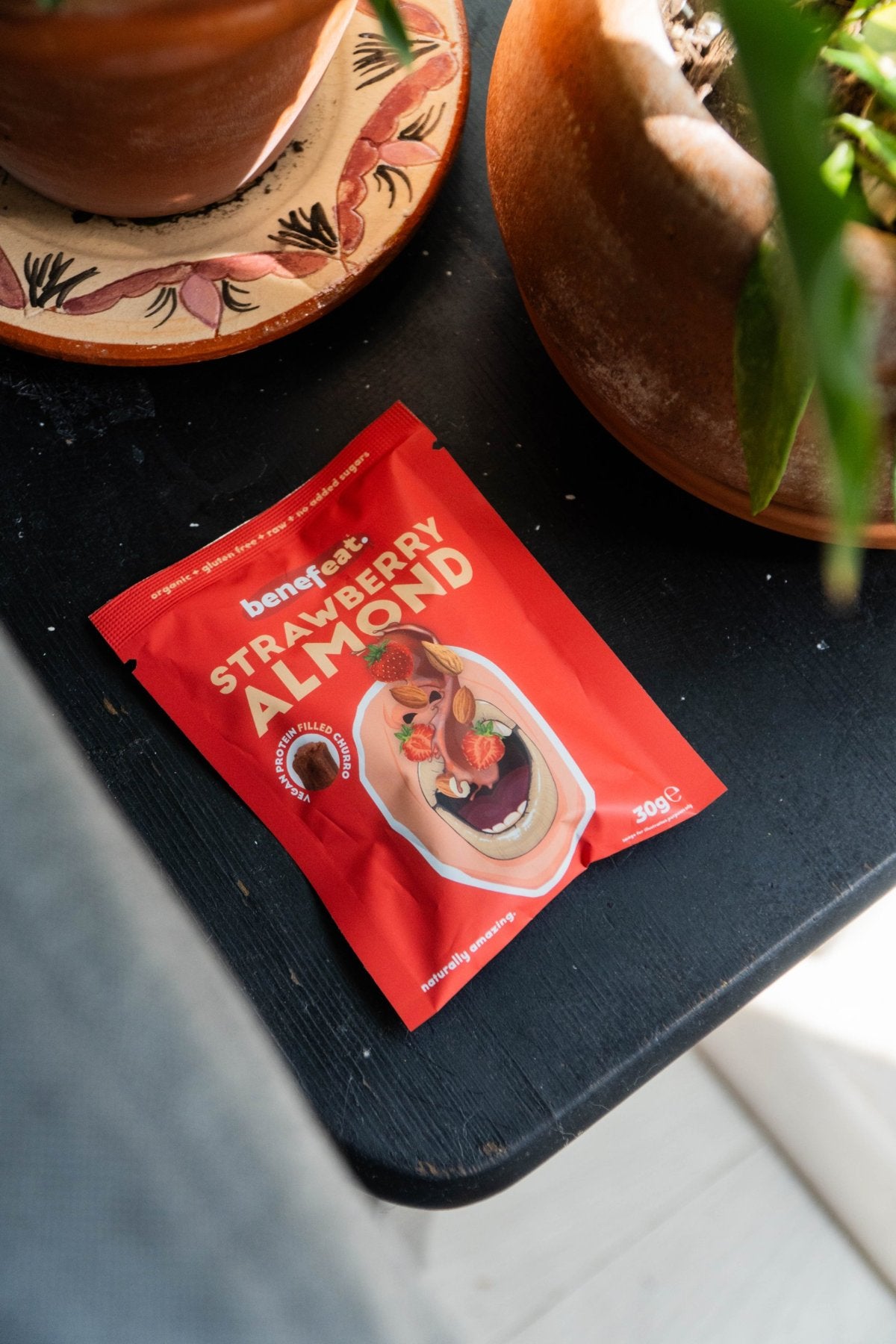 Strawberry Almond pack on a black table between plant pots